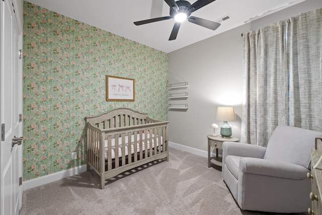 bedroom with light colored carpet, a nursery area, and ceiling fan