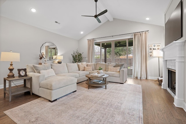 living room with ceiling fan, wood-type flooring, beam ceiling, high vaulted ceiling, and a fireplace