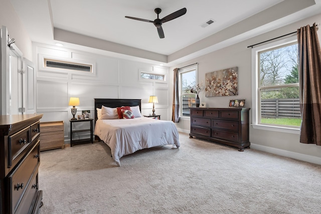 carpeted bedroom featuring ceiling fan, a tray ceiling, and multiple windows