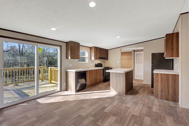 kitchen featuring a textured ceiling, light wood-type flooring, ornamental molding, a kitchen island, and black appliances