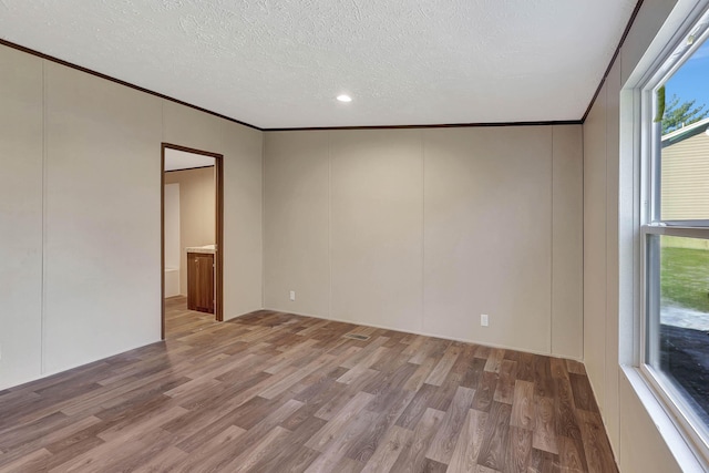 empty room with hardwood / wood-style floors, ornamental molding, and a textured ceiling