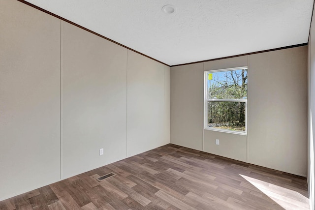 unfurnished room with ornamental molding, a textured ceiling, and light wood-type flooring