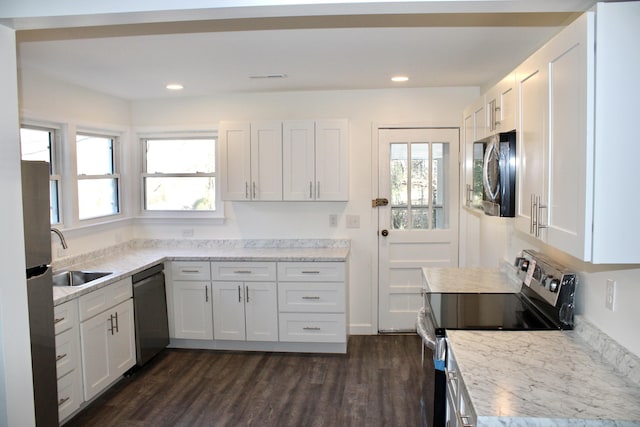 kitchen featuring white cabinets, appliances with stainless steel finishes, light stone counters, and sink