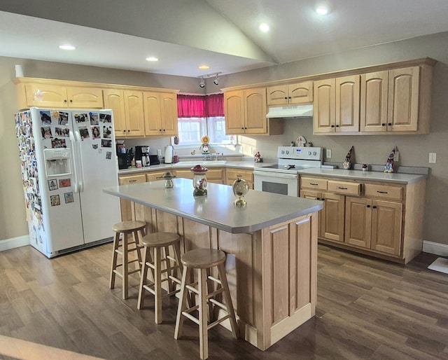 kitchen with white appliances, a center island, a kitchen bar, light brown cabinetry, and lofted ceiling