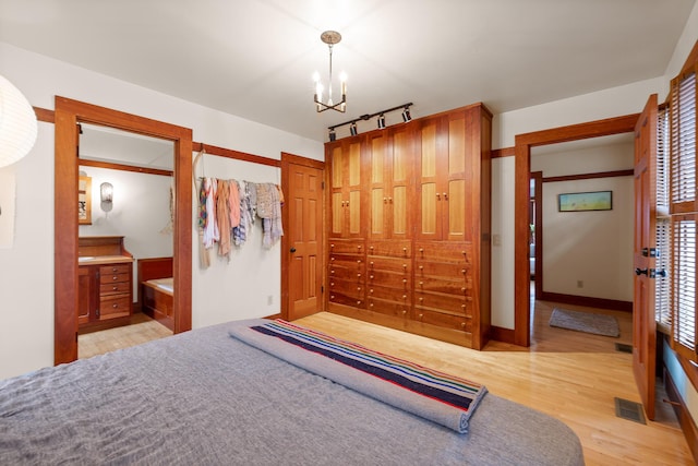 bedroom with rail lighting, light wood-type flooring, connected bathroom, a notable chandelier, and a closet