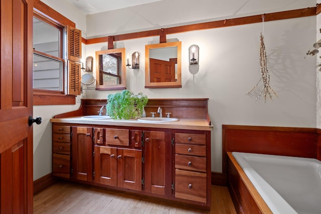 bathroom featuring wood-type flooring, vanity, and tiled bath