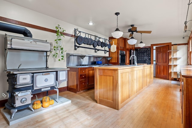 kitchen with sink, a center island with sink, light hardwood / wood-style floors, oven, and hanging light fixtures