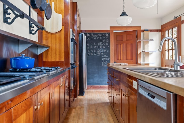 kitchen featuring light wood-type flooring, stainless steel appliances, hanging light fixtures, and sink