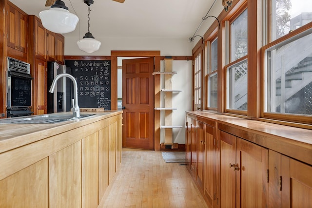 kitchen featuring wooden counters, sink, light hardwood / wood-style flooring, double oven, and decorative light fixtures