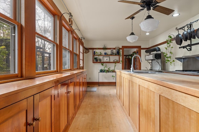 kitchen featuring wooden counters, ceiling fan, sink, light hardwood / wood-style floors, and hanging light fixtures