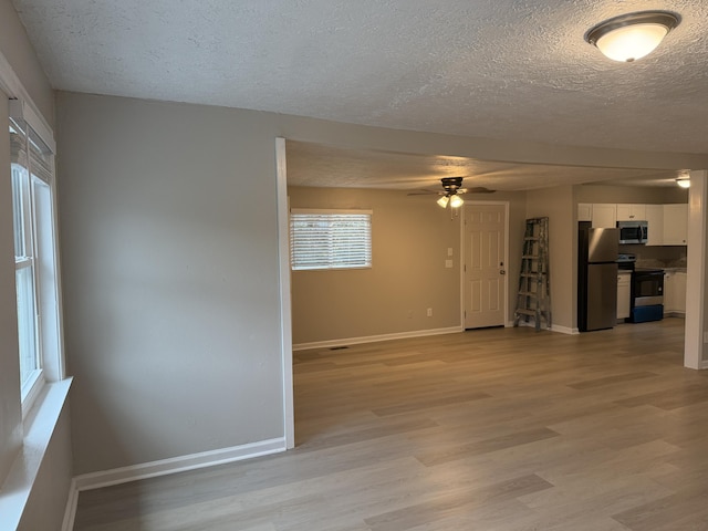 unfurnished room with a textured ceiling, light wood-type flooring, and ceiling fan