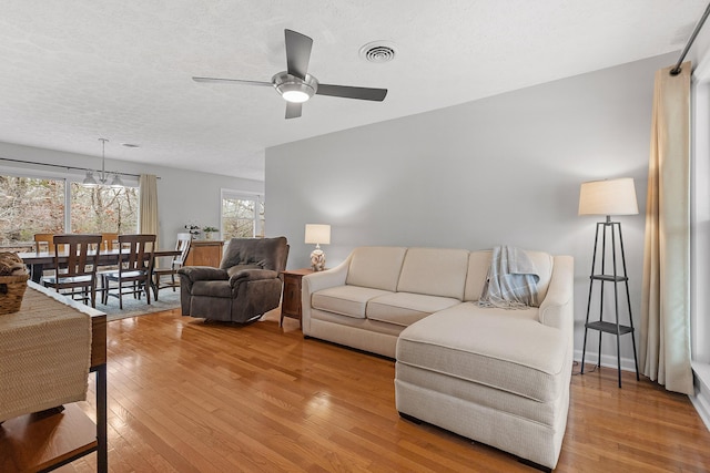 living room featuring a textured ceiling, ceiling fan with notable chandelier, and light hardwood / wood-style floors