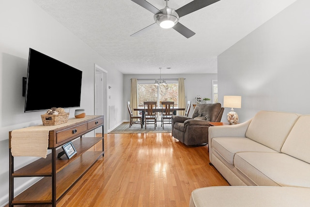 living room with hardwood / wood-style flooring, ceiling fan with notable chandelier, and a textured ceiling