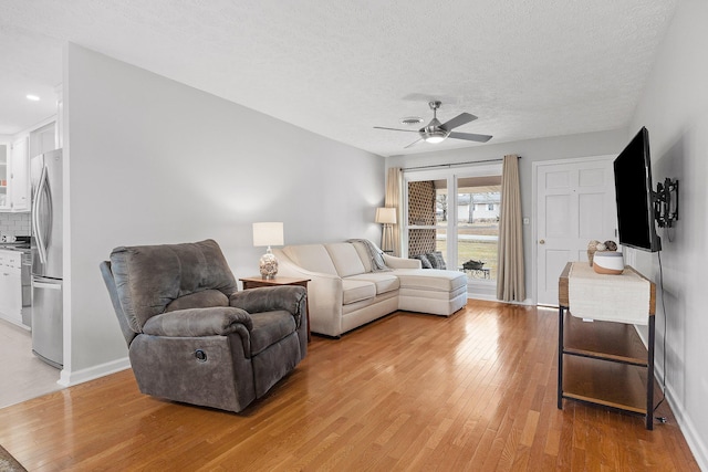 living room featuring ceiling fan, light hardwood / wood-style floors, and a textured ceiling