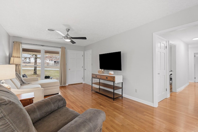 living room featuring ceiling fan, light wood-type flooring, and a textured ceiling