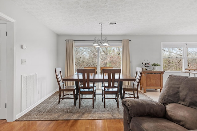 dining area with hardwood / wood-style floors, a healthy amount of sunlight, a textured ceiling, and an inviting chandelier