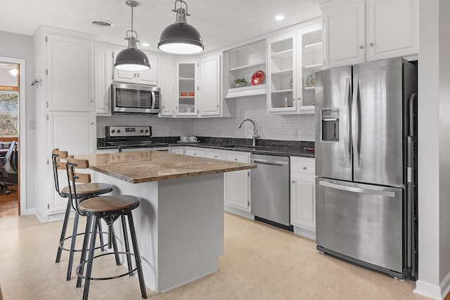 kitchen with appliances with stainless steel finishes, sink, white cabinets, a kitchen island, and hanging light fixtures