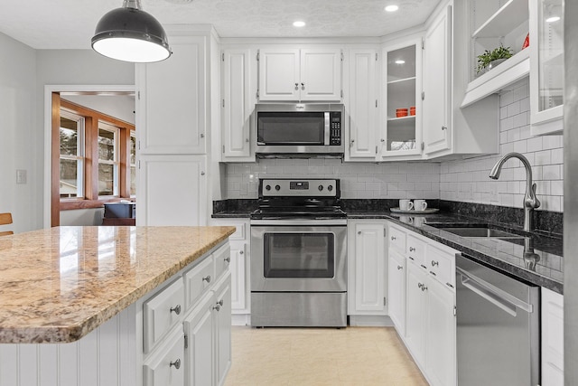 kitchen with white cabinetry, sink, stainless steel appliances, dark stone counters, and pendant lighting