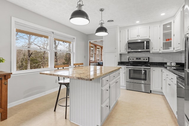 kitchen featuring appliances with stainless steel finishes, tasteful backsplash, pendant lighting, white cabinets, and a center island