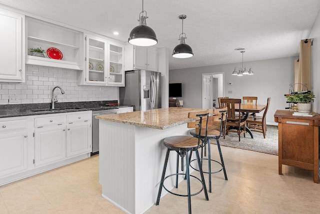 kitchen featuring sink, appliances with stainless steel finishes, decorative light fixtures, a kitchen island, and white cabinetry