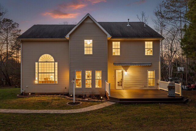 back house at dusk with a wooden deck and a yard