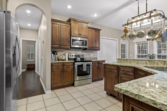 kitchen with tasteful backsplash, appliances with stainless steel finishes, light tile patterned floors, and hanging light fixtures