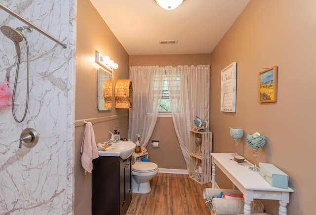 bathroom with hardwood / wood-style floors, vanity, toilet, and tiled shower