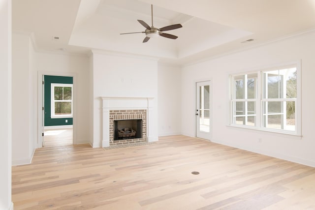 unfurnished living room with plenty of natural light, a raised ceiling, light wood-type flooring, and crown molding