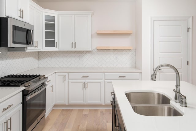 kitchen featuring sink, tasteful backsplash, appliances with stainless steel finishes, white cabinets, and light wood-type flooring