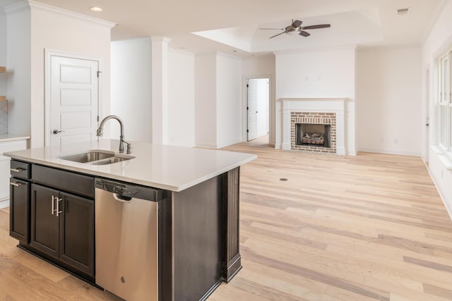 kitchen featuring stainless steel dishwasher, a tray ceiling, sink, a center island with sink, and light hardwood / wood-style floors