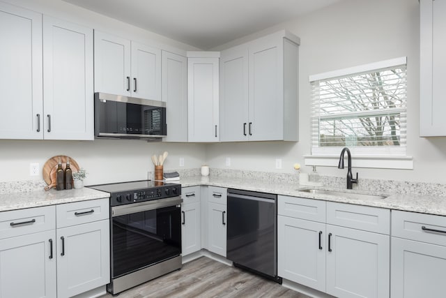 kitchen featuring light hardwood / wood-style floors, light stone counters, sink, and appliances with stainless steel finishes