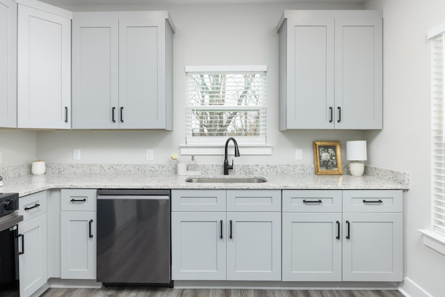 kitchen featuring stainless steel dishwasher, light stone counters, white cabinetry, and sink