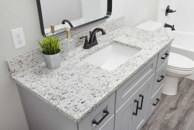 bathroom with hardwood / wood-style floors, vanity, toilet, and a washtub