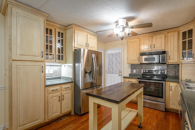 kitchen featuring appliances with stainless steel finishes, tasteful backsplash, a textured ceiling, ceiling fan, and dark hardwood / wood-style floors