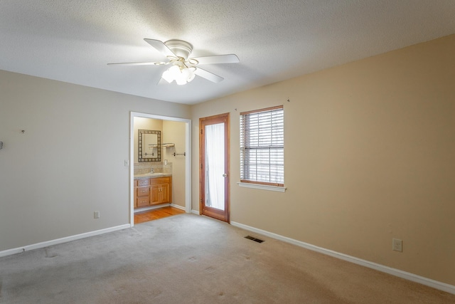 unfurnished bedroom featuring ceiling fan, ensuite bathroom, light colored carpet, and a textured ceiling