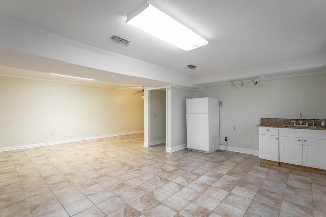 basement with a textured ceiling, white fridge, sink, and rail lighting