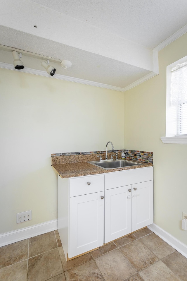 kitchen with white cabinets, a textured ceiling, ornamental molding, and sink