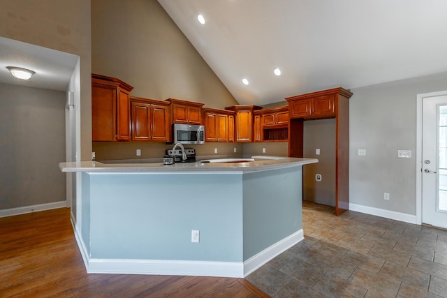 kitchen with baseboards, appliances with stainless steel finishes, brown cabinets, light countertops, and high vaulted ceiling