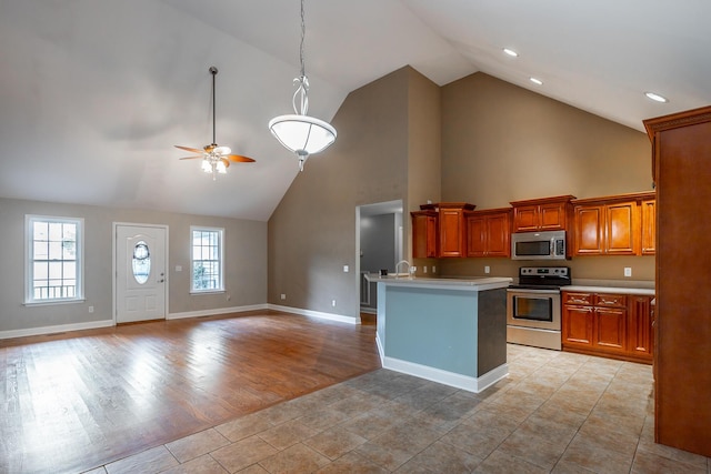 kitchen featuring brown cabinetry, a ceiling fan, open floor plan, stainless steel appliances, and light countertops