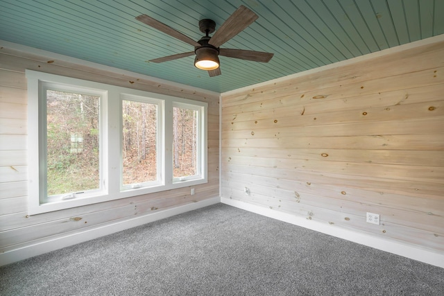 carpeted spare room featuring a ceiling fan, wooden walls, and baseboards