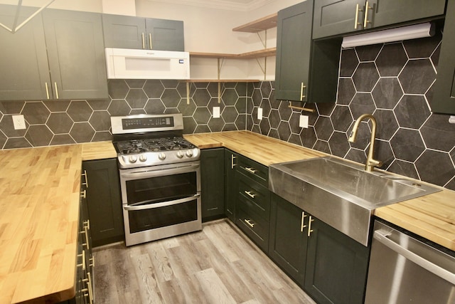 kitchen with tasteful backsplash, butcher block counters, sink, and appliances with stainless steel finishes