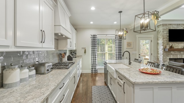 kitchen featuring a kitchen island with sink, pendant lighting, white cabinets, and light stone counters