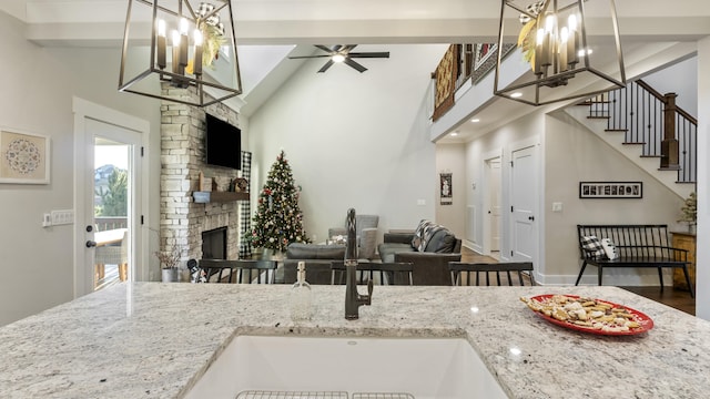 kitchen featuring light stone countertops, a stone fireplace, hanging light fixtures, and sink