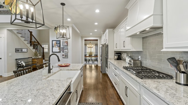 kitchen with light stone countertops, premium range hood, a notable chandelier, white cabinets, and hanging light fixtures