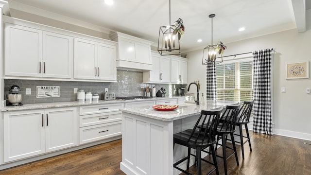 kitchen with light stone counters, dark hardwood / wood-style floors, pendant lighting, a kitchen island with sink, and white cabinets