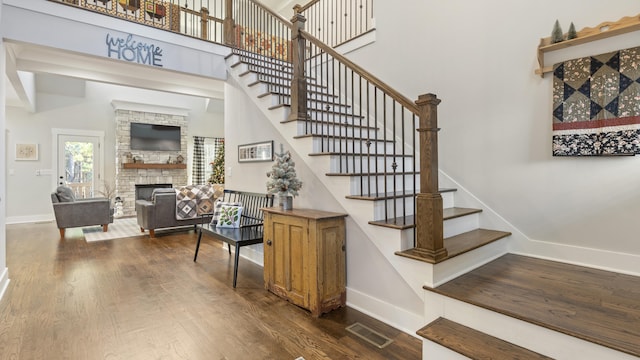 staircase with wood-type flooring, a towering ceiling, and a stone fireplace