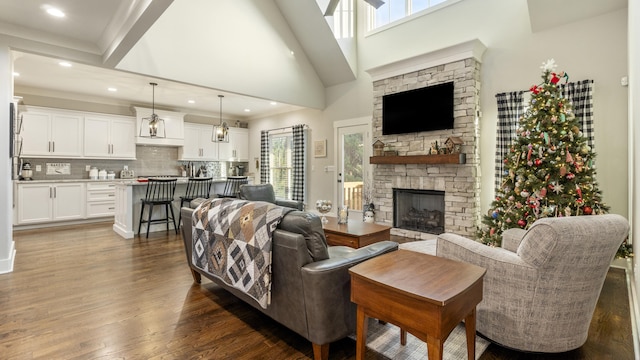 living room with dark hardwood / wood-style flooring, a stone fireplace, a towering ceiling, and a wealth of natural light