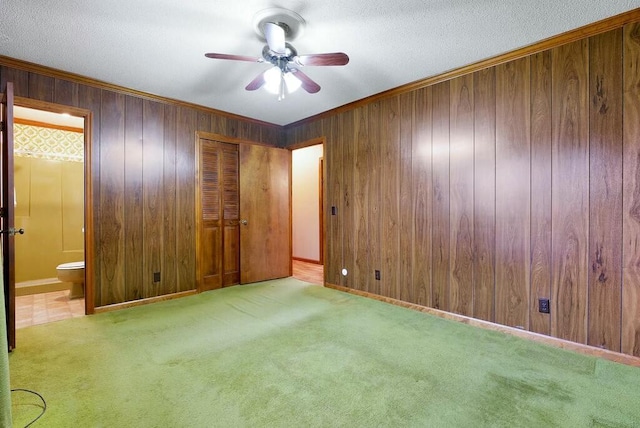 unfurnished bedroom featuring ensuite bath, ceiling fan, wood walls, light colored carpet, and a closet