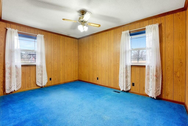 spare room with dark colored carpet, plenty of natural light, ceiling fan, and wooden walls