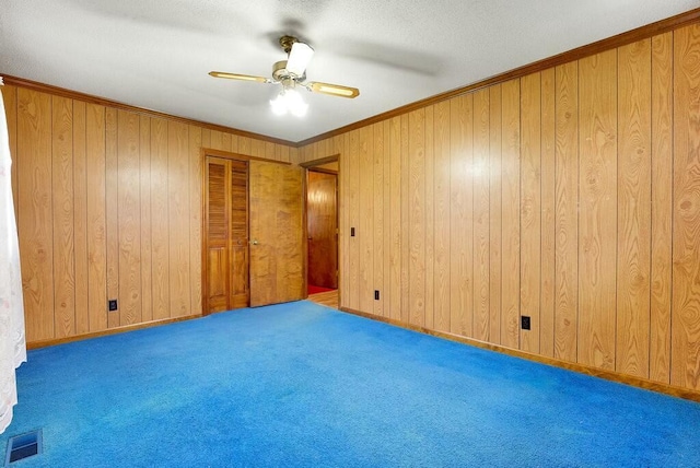 spare room with carpet, ceiling fan, crown molding, and wood walls